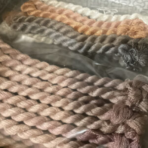 A selection of yarns in neutral and earth tones, arranged to show different textures and thicknesses.