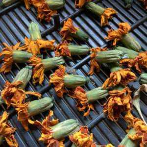 Dried marigold flowers laid out on a metal grate, with a focus on their rich orange hues even in a dried state.